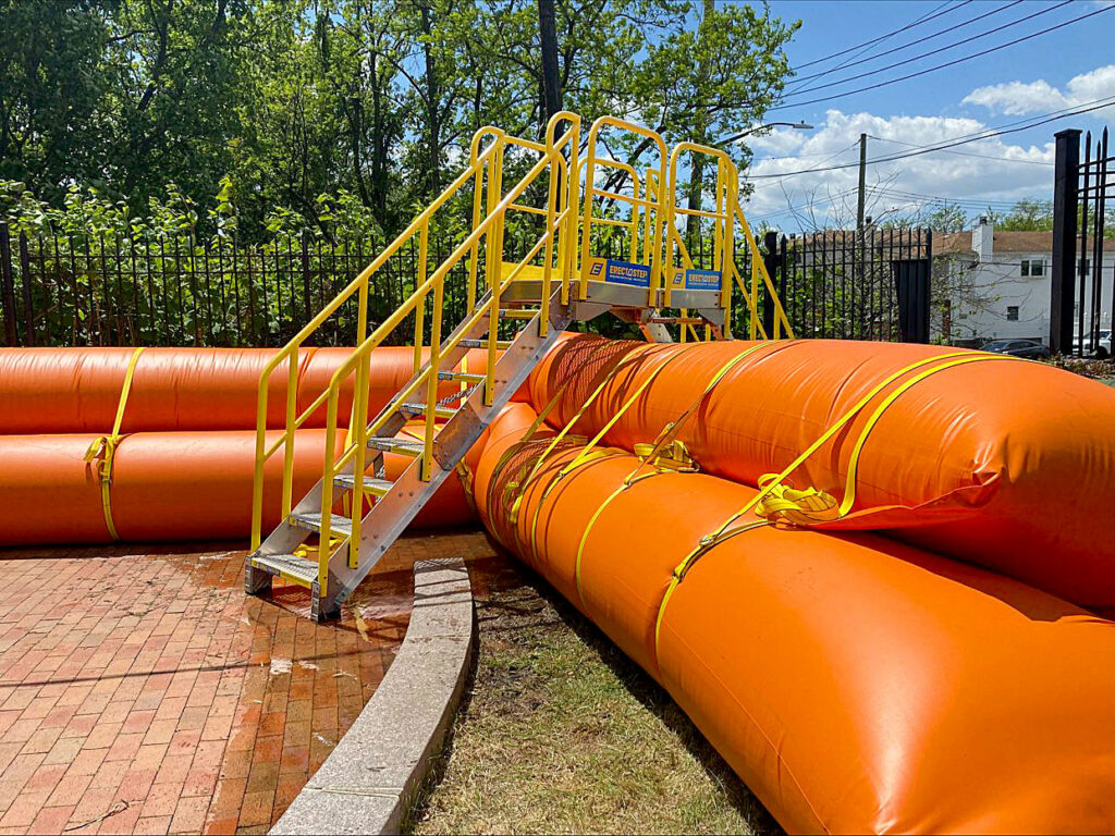 crossover ctairs positioned over tubular, quick-installing, water-filled flood barrier system