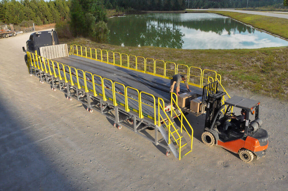 Worker standing on custom rolling platform for flatbed truck outdoors by pond